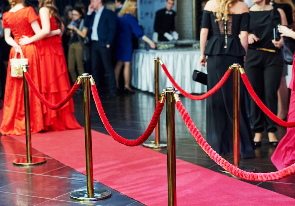event party. red carpet entrance with golden stanchions and ropes. guests in the background